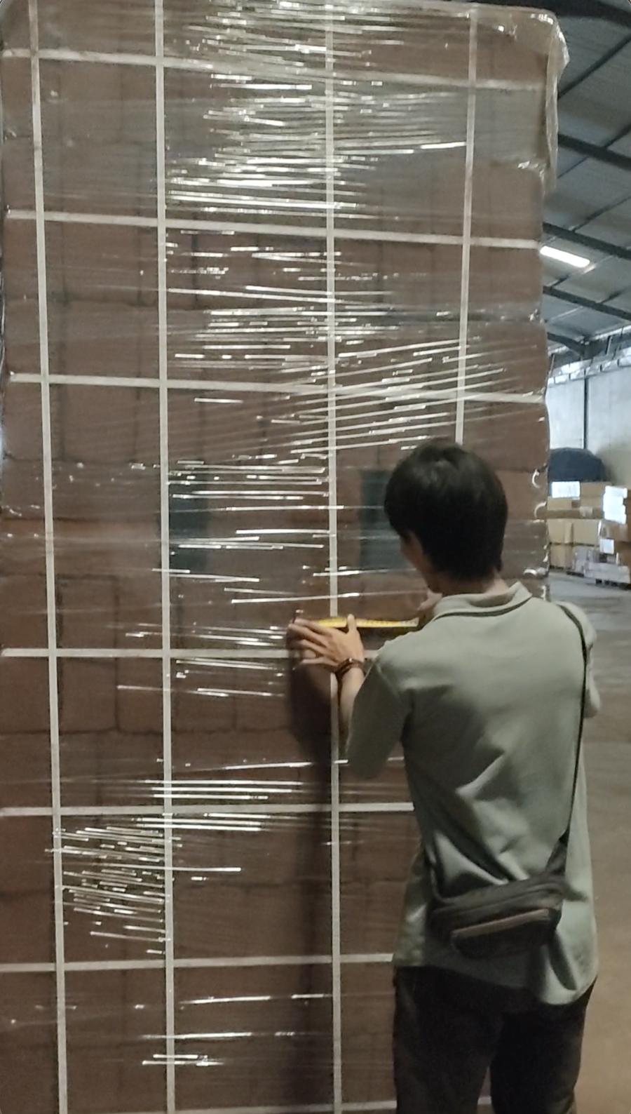 Worker measuring a wrapped pallet of cocopeat blocks